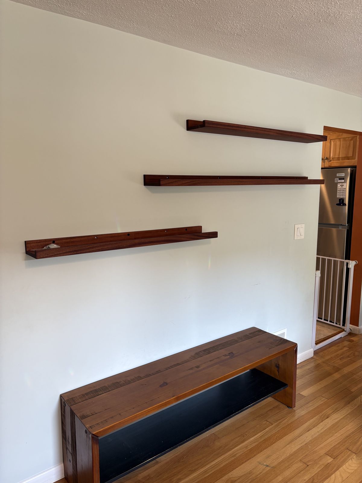 Three staggered dark wood picture-ledge shelves mounted on the wall above a wooden bench