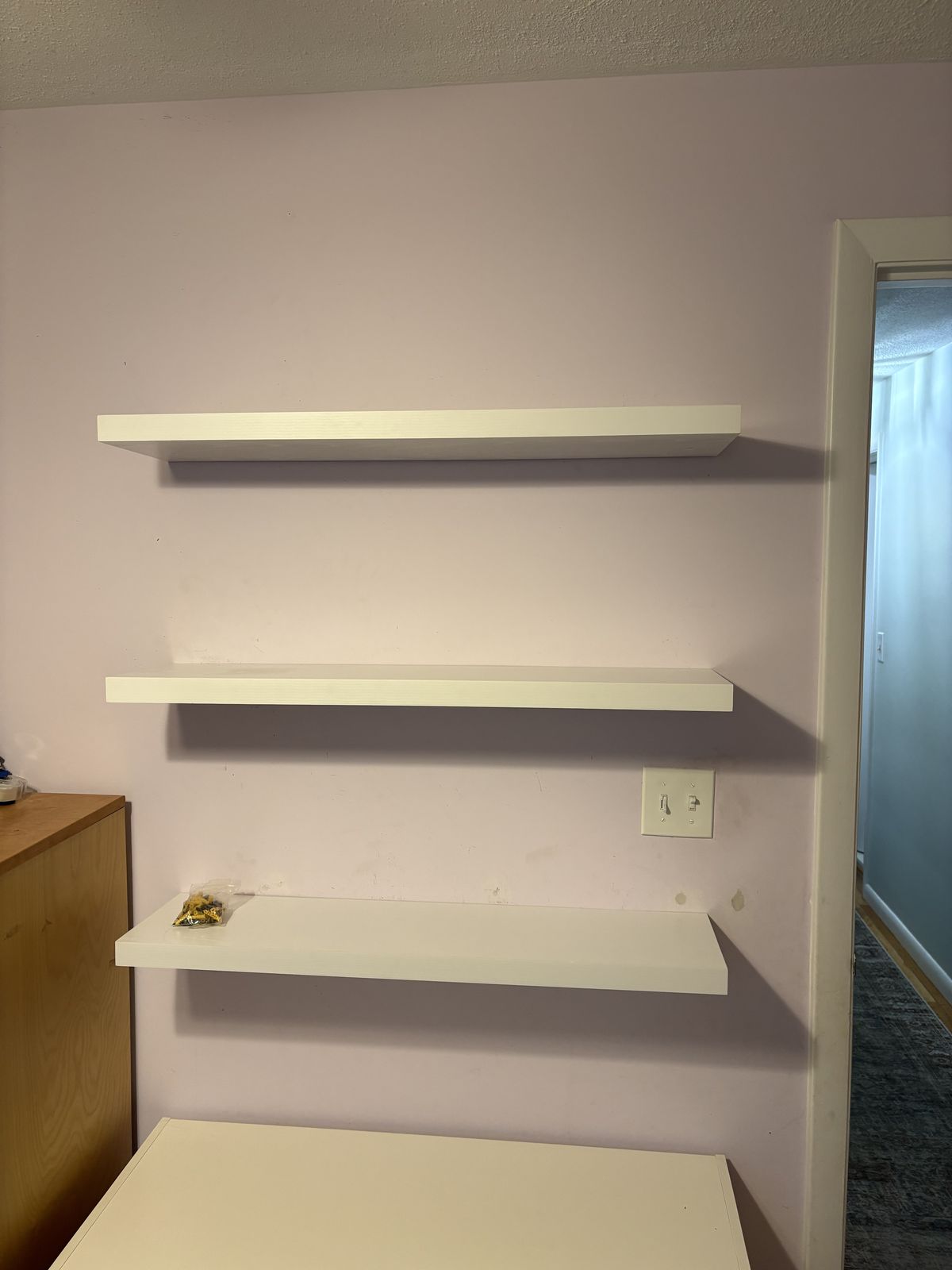 Three white floating shelves mounted evenly on a bedroom wall